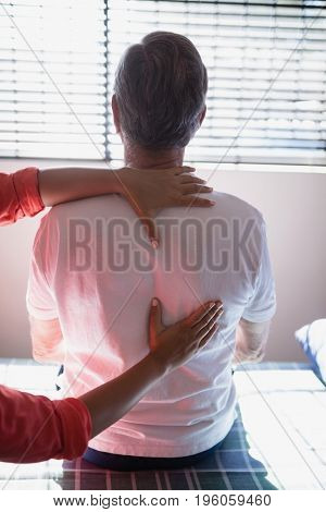 Rear view of senior male patient receiving back massage from female therapist at hospital ward