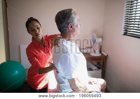 Young female therapist massaging back of senior male patient at hospital ward