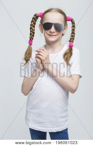 Kids Concepts. Portrait of Positive Caucasian Blond Girl With Pigtails Posing with Artistic Spectacles Against White Background. Vertical Image