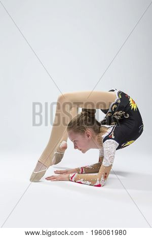Sport Ideas. Young Caucasian Female Rhythmic Gymnast Athlete In Professional Competitive Suit Doing Backbend Stretching Exercise While Posing in Studio Against White. Vertical Image Orientation