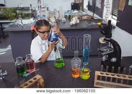 High angle view of elementary student examining blue chemical in flask by desk at science laboratory