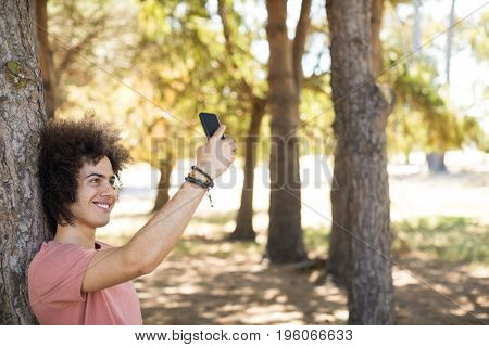 Smiling taking selfie while standing by tree tunk at forest