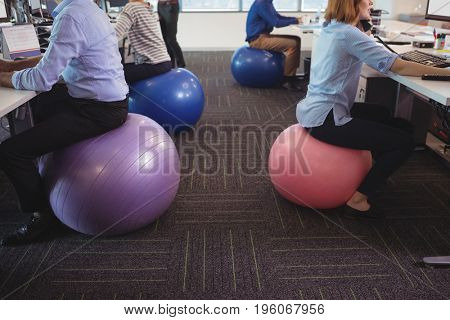 Low section of business people sitting on exercise balls while working at desk in office