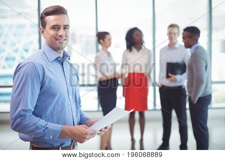 Smiling businessman holding documets with colleagues standing in background at office