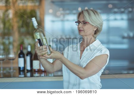 Businesswoman looking at winebottle while standing in office