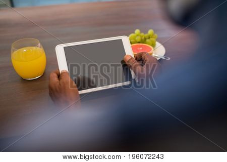 Cropped image of senior man using tablet while sitting at table