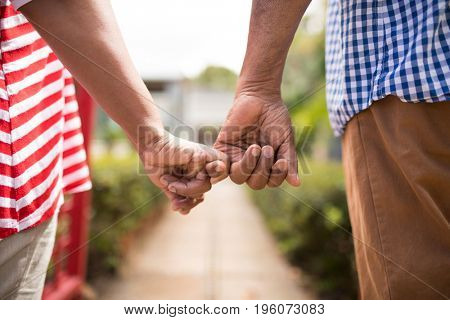 Cropped image of senior couple holding little fingers while standing in yard