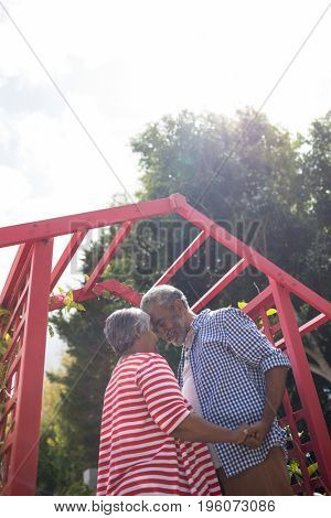 Low angle view of affectionate senior couple standing by metallic structure in yard against sky