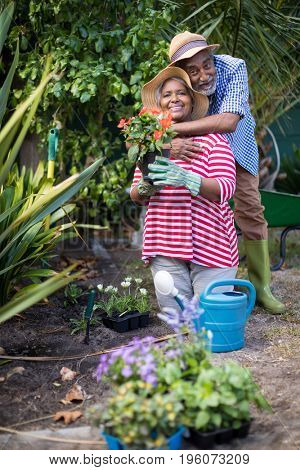 Man embracing woman kneeling on field during gardening in yard 