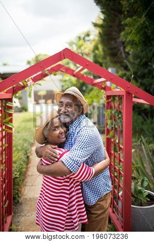 Portrait of senior couple embracing while standing by metallic structure in yard