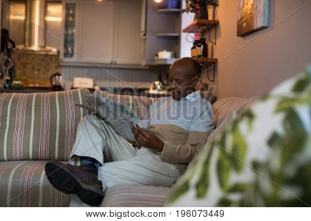 Senior man reading newspaper while sitting on sofa at home