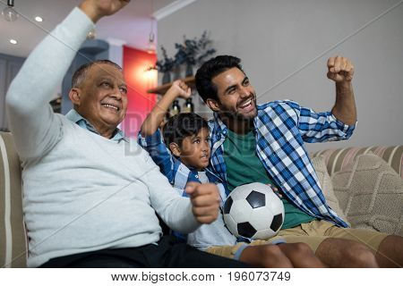 Happy family with arms raised watching soccer match while sitting on sofa at home