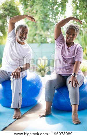 Full length of senior couple exercising while sitting on fitness ball in yard