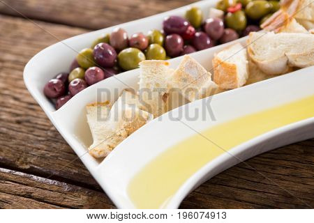 Close-up of marinated olives, bread pieces and olive oil in platter