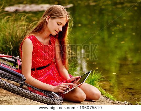Bikes cycling girl wearing red polka dots dress recreation near bicycle into park. Children watch tablet pc in ecotourism. Femle went into social network in campaign. First love.