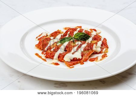 Ravioli with tomato sauce served in white plate on marble serface.