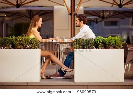 Playful Girlfriend Is Flirting With Guy By Her Leg, Lovers Are Sitting In Light Cafe On A Sunny Day