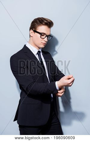 Young Handsome Businessman Lawyer In A Suit Is Fixing His Cuffl Inks, He Stands On Pure Light Backgr
