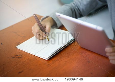 Beautiful Asian Businesswoman Is Taking Notes On Her Notebook While Using The Tablet In Her Office.