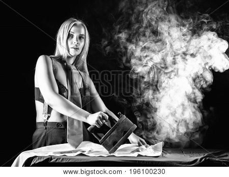 sexy blonde woman in men's pants and a bra, ironing white shirt with old iron. retro style, black and white.