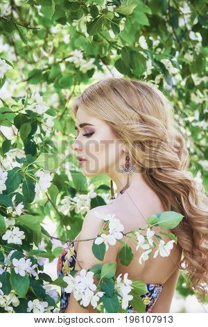 Outdoor fashion beautiful young woman surrounded by lilac flowers summer. Spring blossom lilac bush. Portrait of a girl blondes