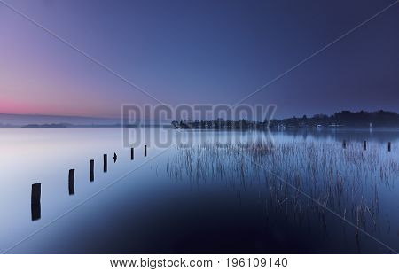 Poles and reed in a mystic morning lake under a blue and red dawn