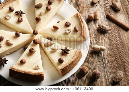 Delicious sliced cheesecake with nuts on wooden table
