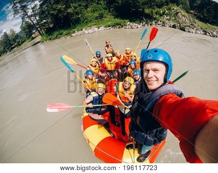 mountain Altai, RUSSIA - July 16, 2017: man in a helmet holds an action camera and makes selfie on the background of friends with oars, rafting