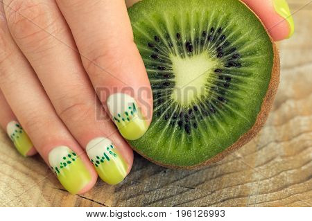 Kiwi and skin care of a beauty female hand with green and white moon nail art manicure on a wooden background