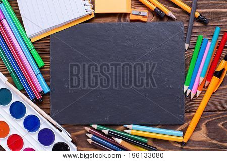 Back to school. Different stationery - pencils pen note erazer paint and empty slate board on wooden background. Top view. Place for text.