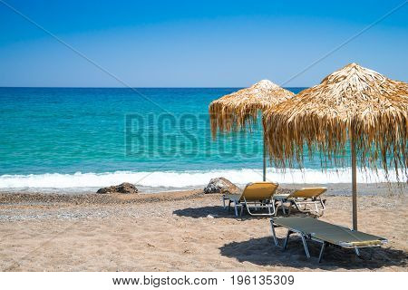 Two straw umbrellas with three sunbeds on the beach Crete Greece