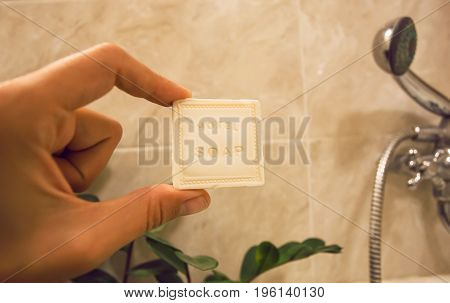 Inside the bathroom of hotel shower andone hand of a visitor holding small piece of bathe soap from toiletries.