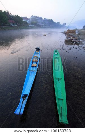 a blue boat and a green boat float side by side in a small river.