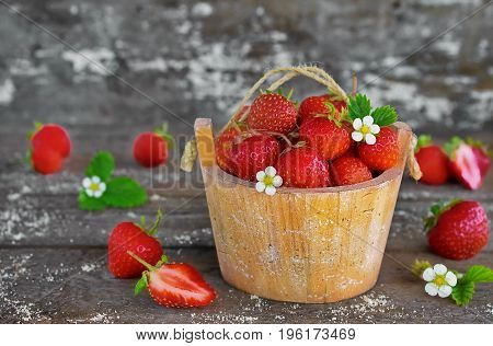 strawberries in a basket on an old wooden background with fresh berries and flowering strawberries