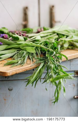Assortment of fresh herbs mint, oregano, thym, blooming sage on cutting board over old blue white wooden kitchen table. Rustic style, day light.