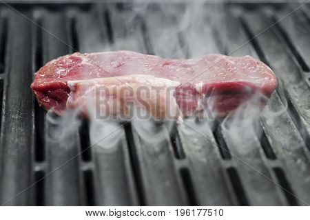 Still raw beef is lying in the smoke on a grill