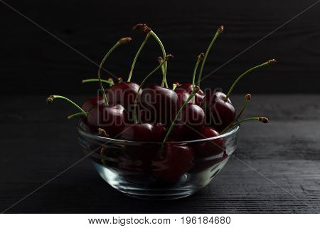 Cherry In A Glass Plate On A Black Wooden Background