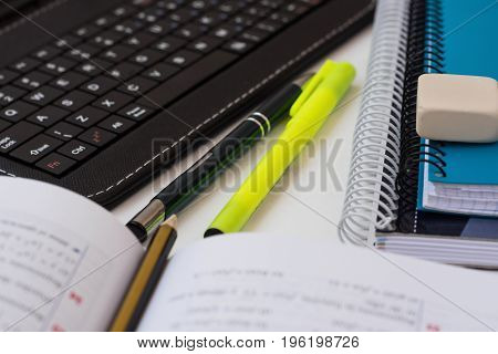 Laptop tablet keyboard opened textbook with math formula pencil stack of school notebooks highlighter on white desktop learning studying education college