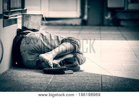 Homeless barefoot man sleep on the street, in the shadow of the building. Social documentary.