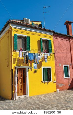 Burano, Italy - May 08, 2013. View of colorful terraced houses and clothes hanging in an alley on sunny day in Burano, a gracious little town full of canals, near Venice. Veneto region, northern Italy