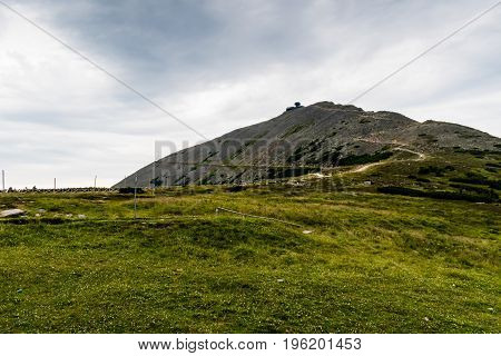 The road leading to the Snezka the highest mountain in Czech. Around the clear green meadow the cloudy sky is very dramatic. The observatory is well visible at the top.