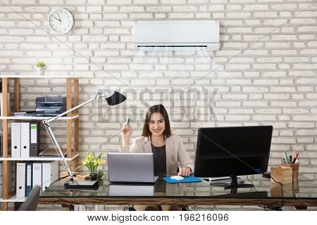Young Businesswoman Operating Air Conditioner With Remote Controller In Office