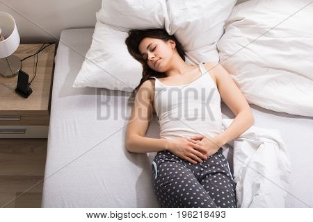 Elevated View Of A Woman Lying On Bed Having Stomach Pain