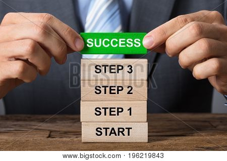 Closeup of businessman building success concept with wooden blocks on wood