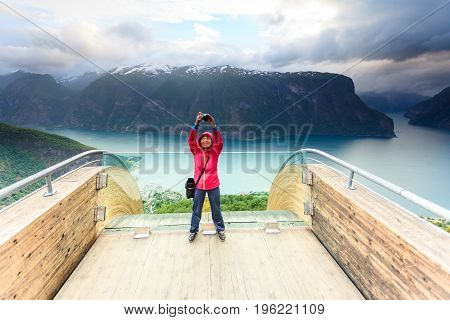 Tourism and travel. Woman tourist nature photographer taking photo with camera enjoying Aurland fjord landscape from Stegastein lookout Norway Scandinavia.