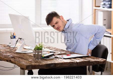 Sad Businessman Sitting On Chair Having Back Pain In Office