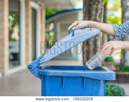 Closeup portrait woman hand throwing empty plastic water bottle in recycling bin.