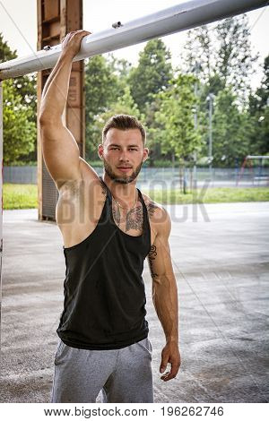 Handsome Muscular Hunk Man Outdoor in City Setting. Showing Healthy Body While Looking Away, Hanging from Bar