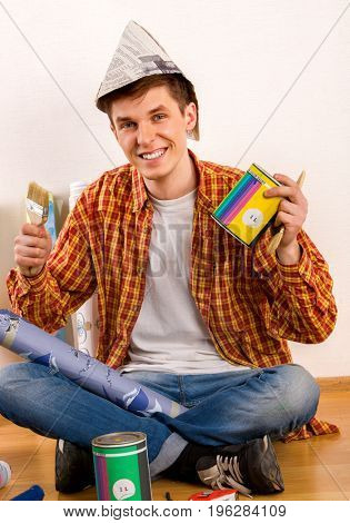 Repair home man holding paint roller for wallpaper. Male in newspaper cap renovation apartment. Student received his own apartment and take paint can and roll paper number one.