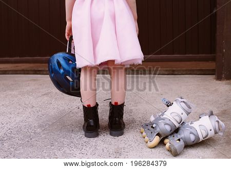 Inline skates sport conceptual image. Active outdoor sport for kids. Young girl is holding a helmet for roller skating in a pink fluffy skirt, at the feet lie roller skates.